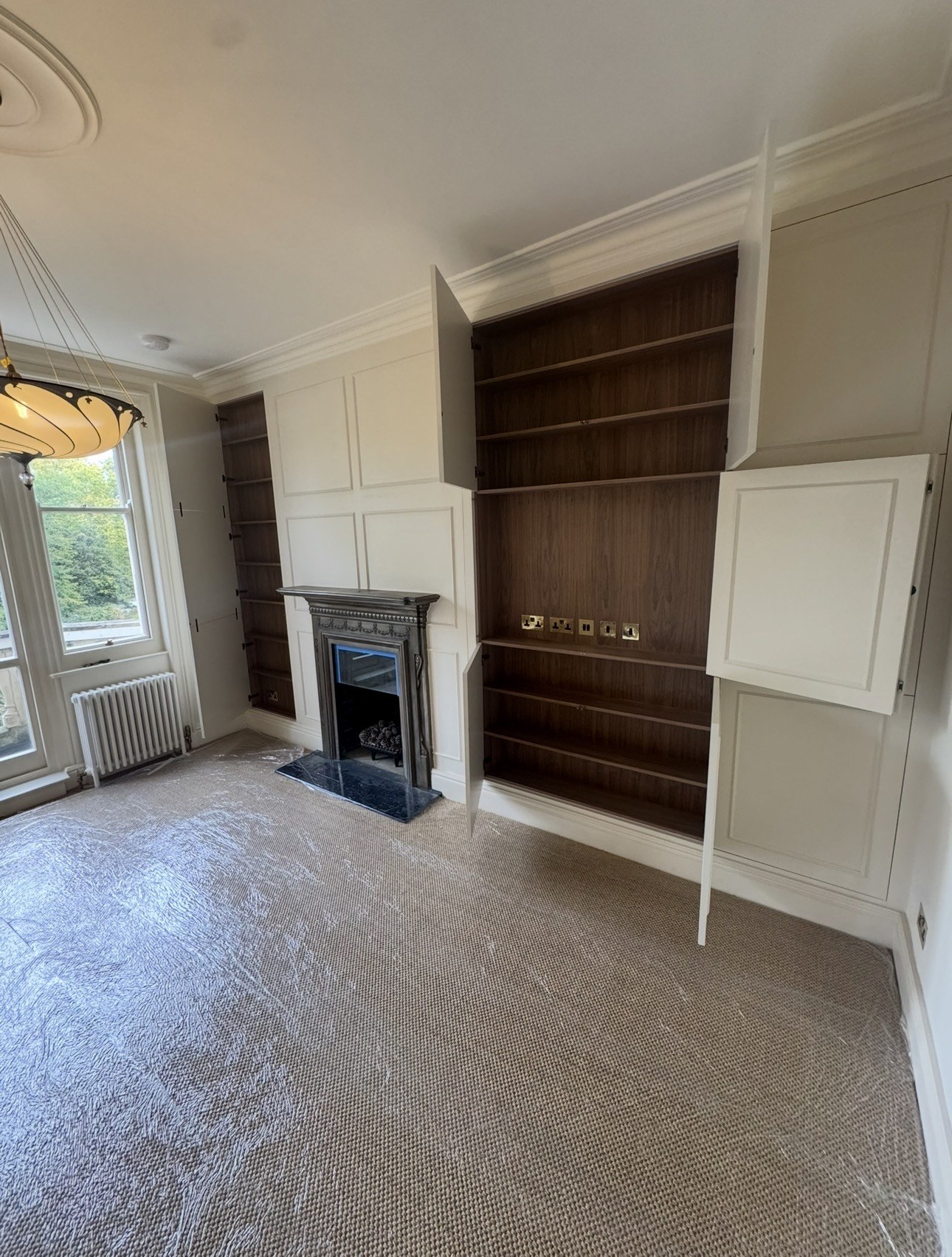 Open walnut veneer shelving behind the period-style panelled media wall