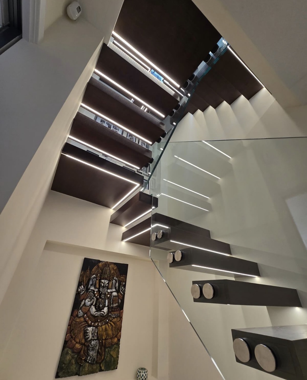 Low-angle view beneath illuminated oak treads and glass balustrade