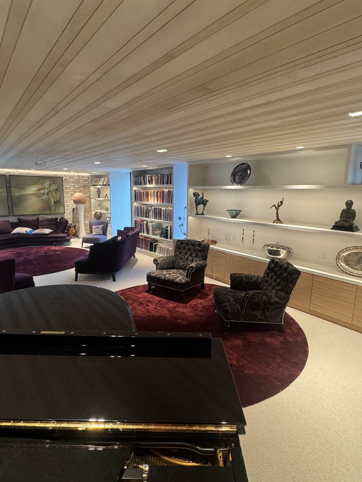 Piano and seating beneath the bespoke ceiling, with LED-lit shelves and low-level drawers
