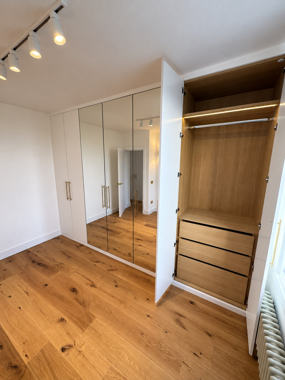 Open wardrobe in bedroom two showing Sorano oak MFC drawers and LED-lit hanging space