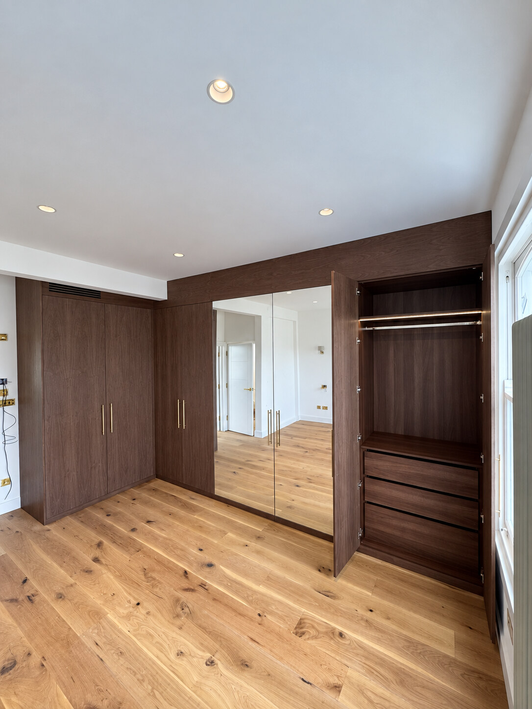Open walnut wardrobe showing walnut MFC drawers, hanging space and LED lighting