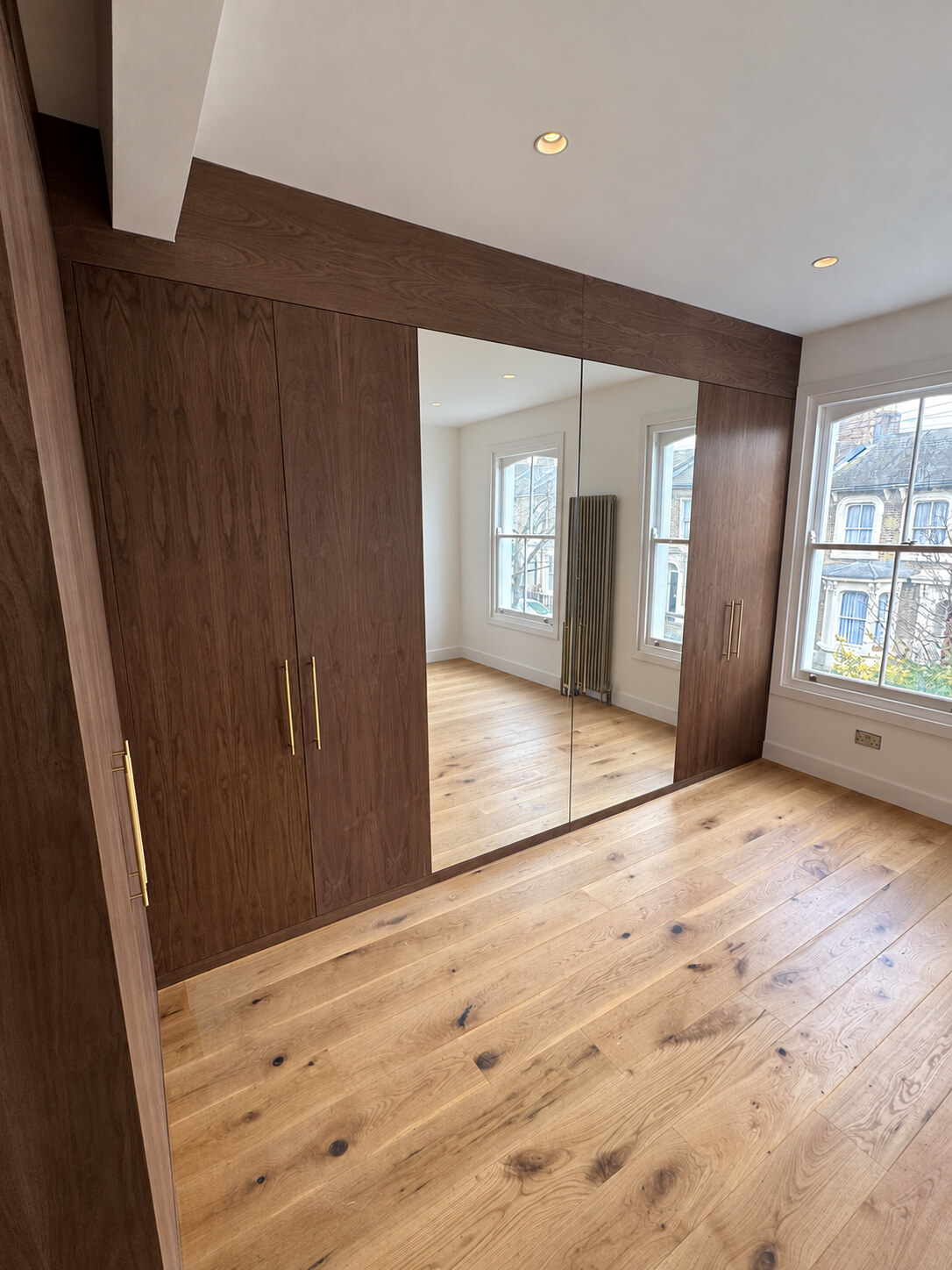 Another angle of the L-shaped walnut veneer master wardrobe with mirrored doors