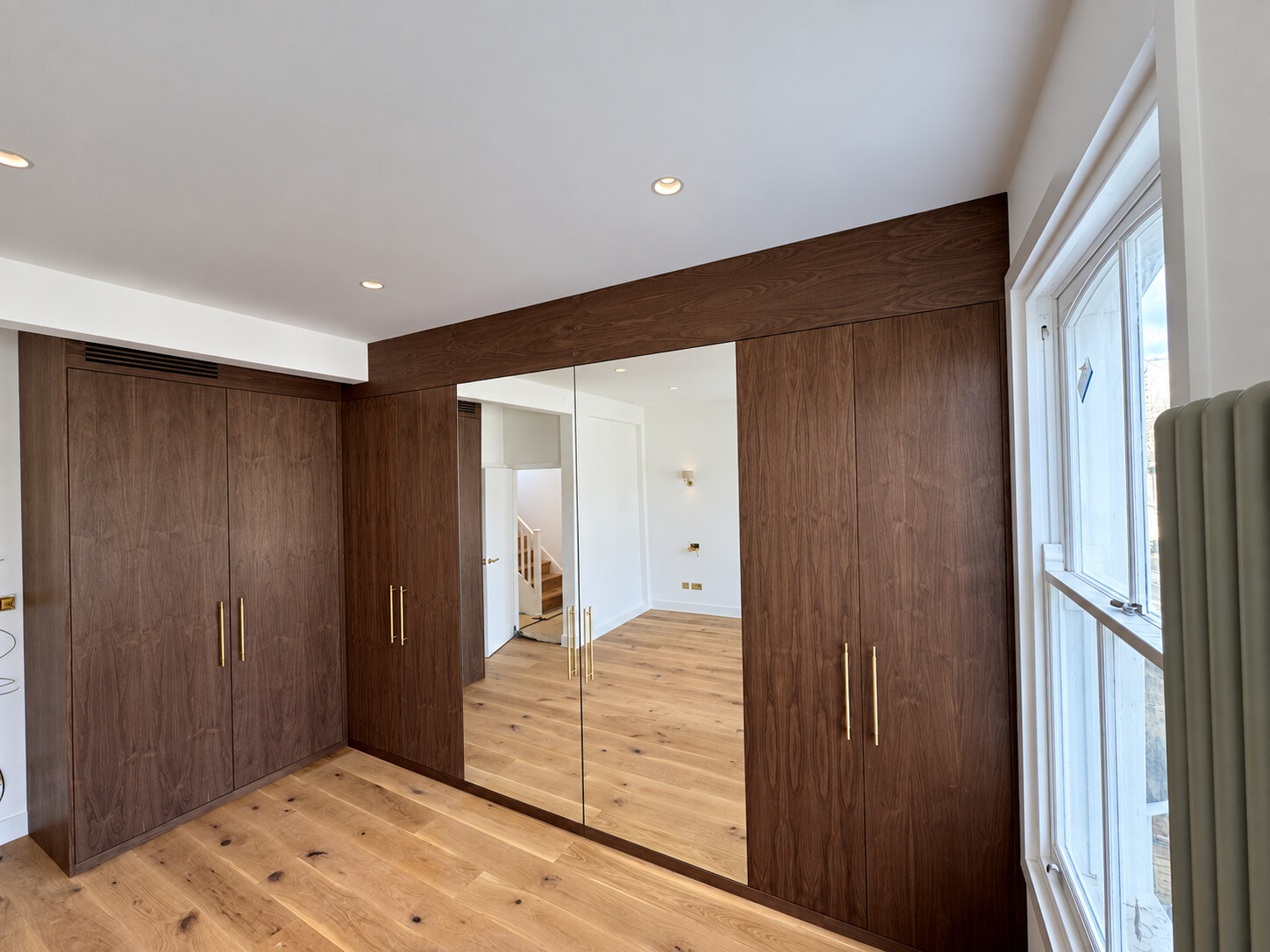 L-shaped walnut veneer wardrobes with two mirrored doors in the master bedroom