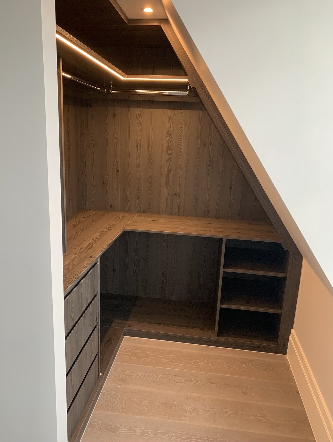 Fitted dark oak storage beneath a sloping ceiling with LED lighting