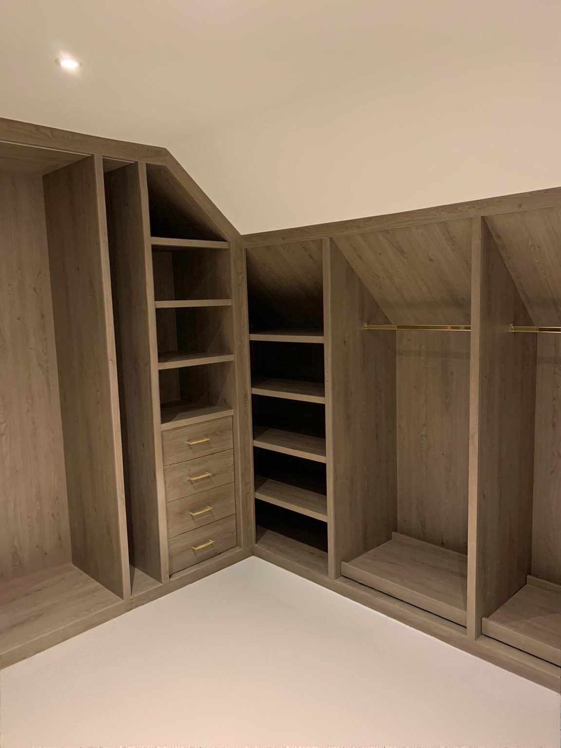 Fitted walk-in wardrobe turning the corner beneath a sloped ceiling, with open shelves and brass hanging rails