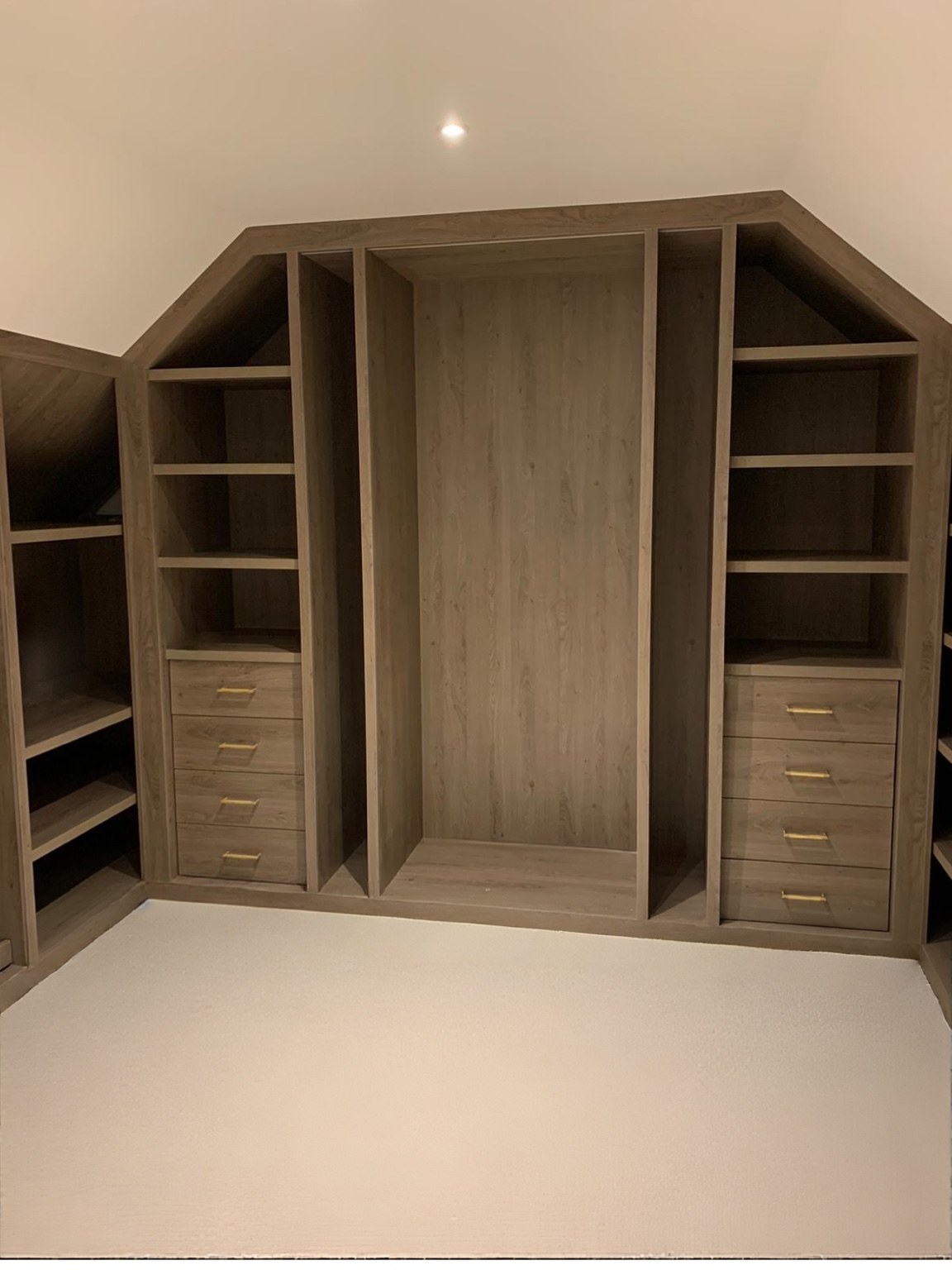 Door-free walk-in wardrobe with fitted shelving and drawers beneath the sloping roof